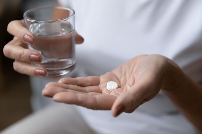 close up of a woman holding an aspirin pill in one hand and a glass of water in the other