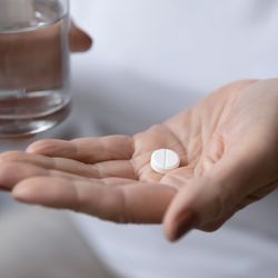 close up of a woman holding an aspirin pill in one hand and a glass of water in the other