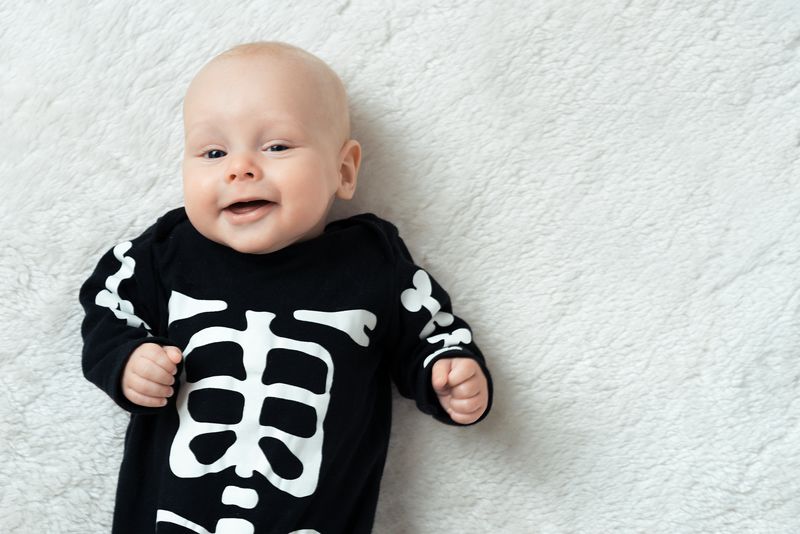 baby lying on a white carpet wearing a black and white skeleton halloween costume