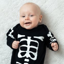 baby lying on a white carpet wearing a black and white skeleton halloween costume