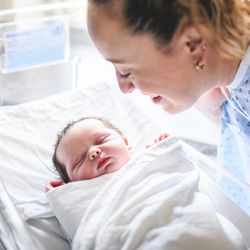 newborn baby sleeping in a hospital cot, mother looking over