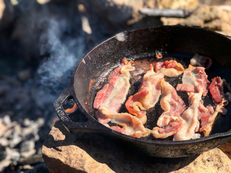 Fried bacon in a cast iron pan cooking over fire