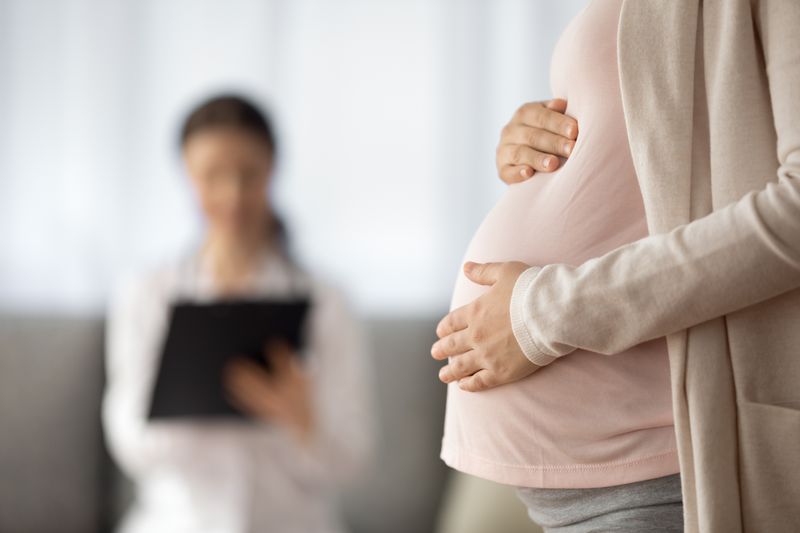  Close up of woman expecting baby having appointment with doctor, her hands are holding the baby bump