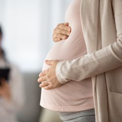  Close up of woman expecting baby having appointment with doctor, her hands are holding the baby bump