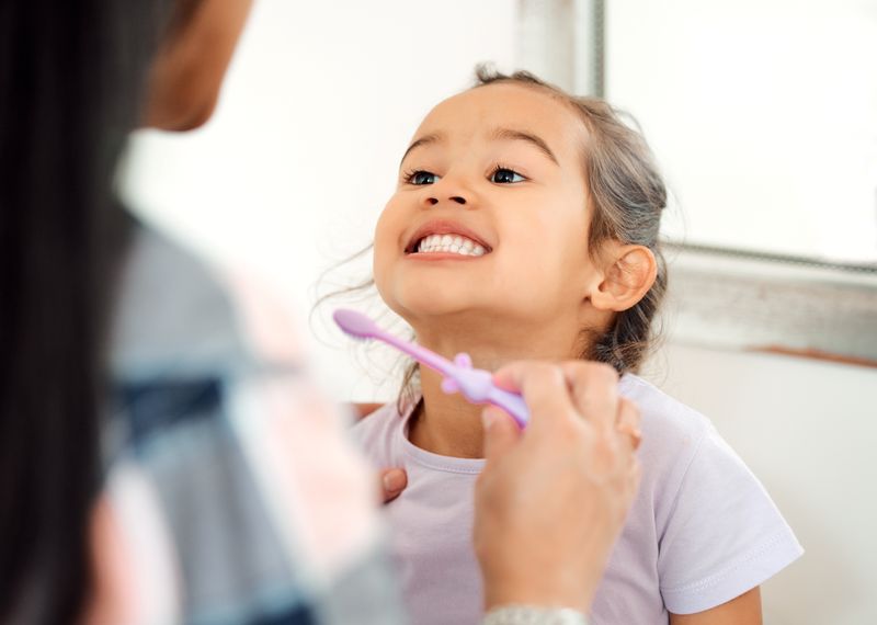 young girl smiling while mother brushes her teeth