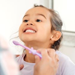 young girl smiling while mother brushes her teeth