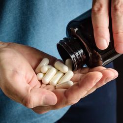 Person pouring white pills into their hand out of a brown glass bottle