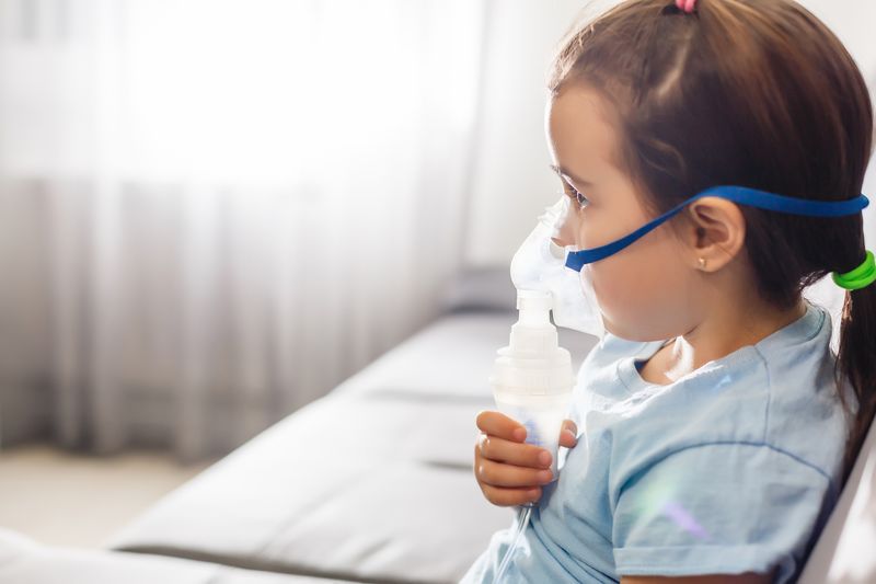 young girl sitting on a sofa and receiving medication via a nebuliser