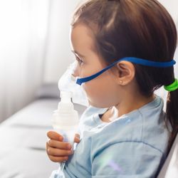 young girl sitting on a sofa and receiving medication via a nebuliser
