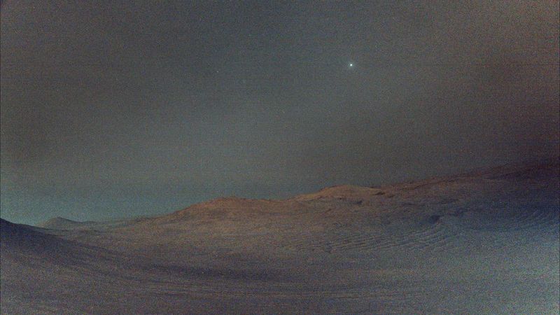 The martian terrain is poorly illuminated an hazy and in the sky a bright dot and a few more dots here and there, not all stars.