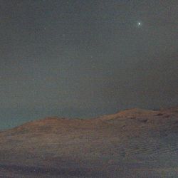 The martian terrain is poorly illuminated an hazy and in the sky a bright dot and a few more dots here and there, not all stars.