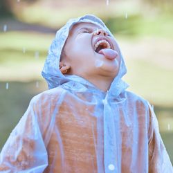 kid standing outside wearing a raincoat with mouth open and tongue out, trying to drink the rain