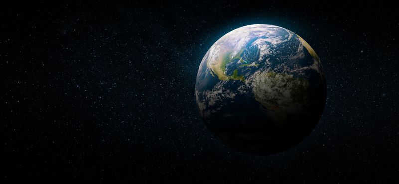 A view of Earth from space showing North and South America with clouds and sunlight visible, surrounded by a dark star-filled background.
