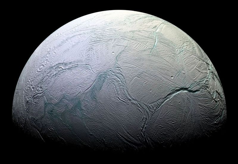 A quarter of enceladus is visible. the icy surface is marked by deep, long, and sinous canyons
