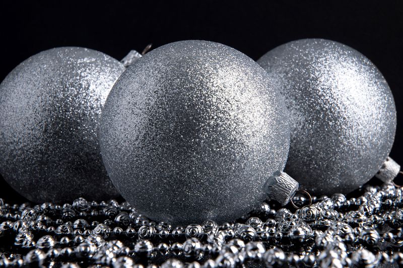 Three silver glitter balls baubles Christmas decoration on a black background on silver beads