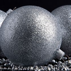 Three silver glitter balls baubles Christmas decoration on a black background on silver beads