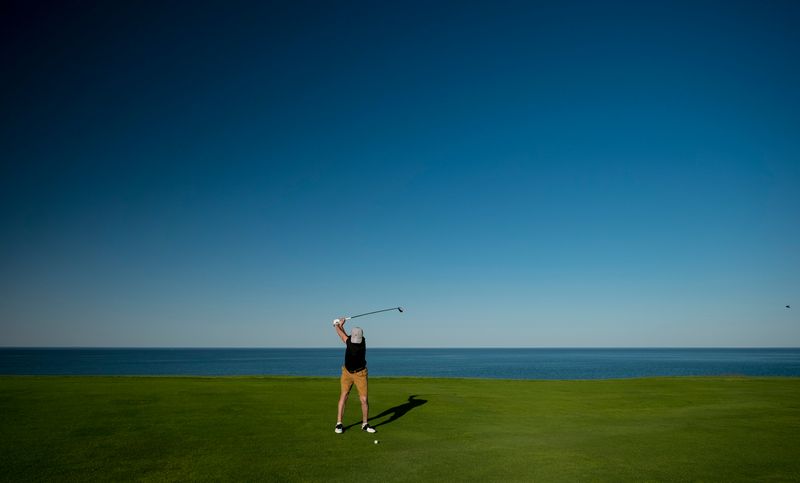 Many swinging a golf club on a green, blue sky behind