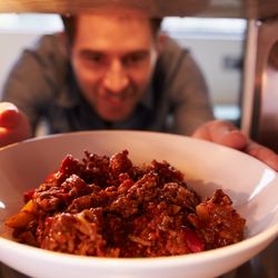 Man Putting Leftover Chili Into Microwave Oven To Cook
