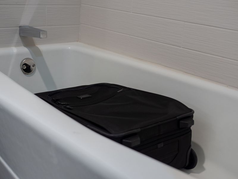 A black suitcase placed flat in a white hotel bathtub