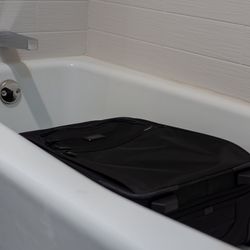 A black suitcase placed flat in a white hotel bathtub