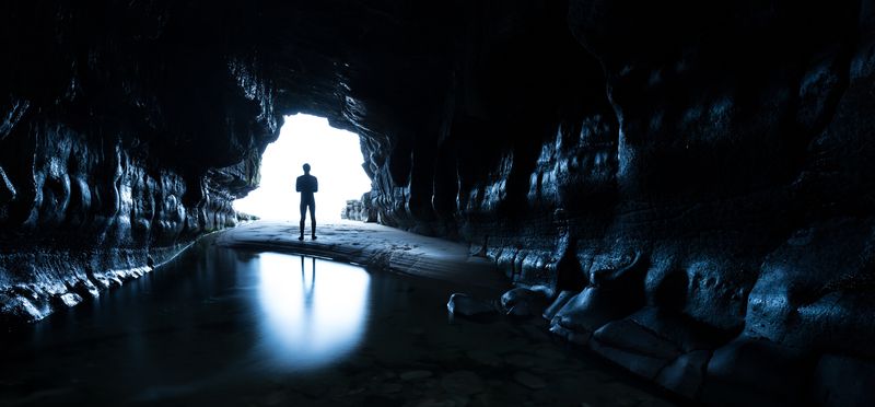 Man standing at the entrance of a dark cave, silhouetted by light
