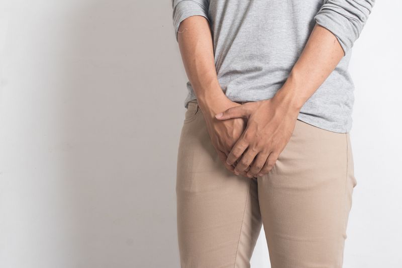 Male in a grey sweatshirt and beige pants covering his crotch. 