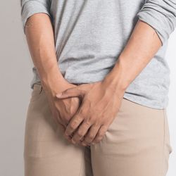 Male in a grey sweatshirt and beige pants covering his crotch. 