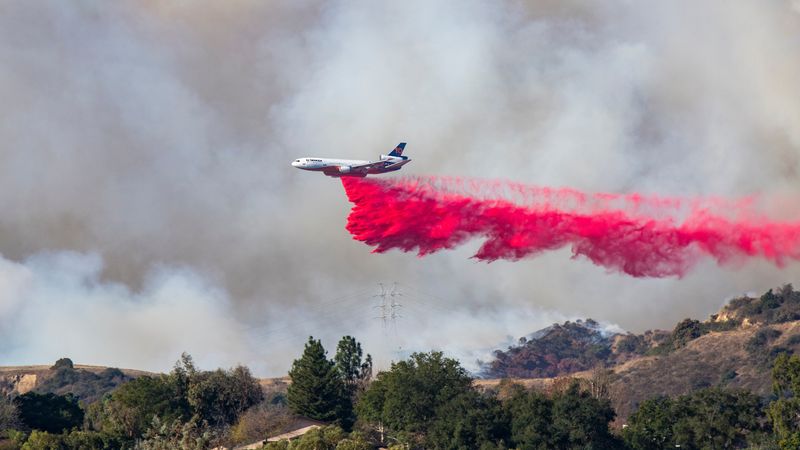 A plane flying across a smoky sky and dropping fire retardant on the Palisades Fire, January 11, 2025.