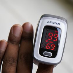 close up of a pulse oximeter clipped onto the finger of a person with a darker skin tone