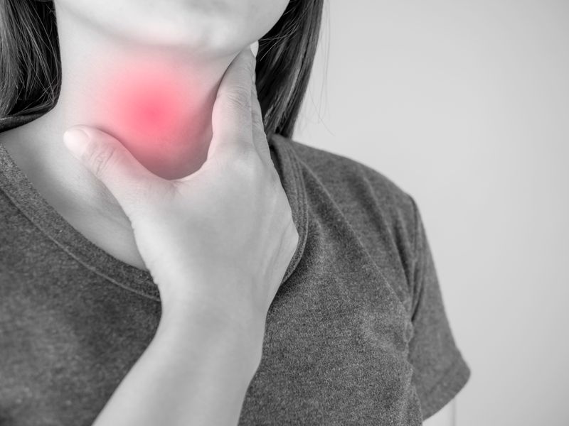 black and white close up of a woman holding her throat, with red overlay to indicate pain