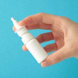 Hand holds a bottle of nasal spray on blue background. 