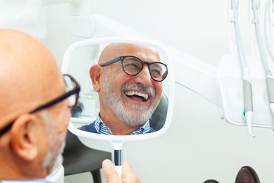 happy older man holding a mirror in his hand at the dental clinic