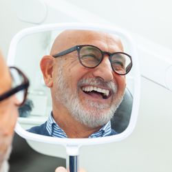 happy older man holding a mirror in his hand at the dental clinic