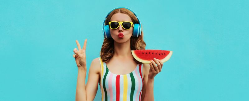 woman in headphones and sunglasses holding a slice of watermelon and making a peace sign