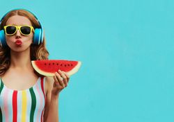 woman in headphones and sunglasses holding a slice of watermelon and making a peace sign