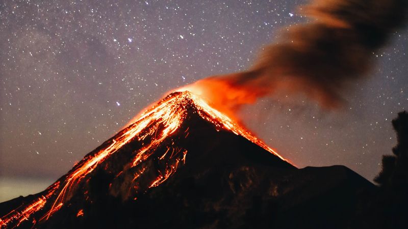 A vertical shot of the volcanic mountain Feugo erupting at night by a starry sky in the background