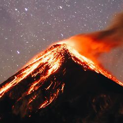A vertical shot of the volcanic mountain Feugo erupting at night by a starry sky in the background