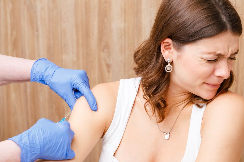 close up of woman flinching away and looking scared while doctor gives her an injection in the upper arm