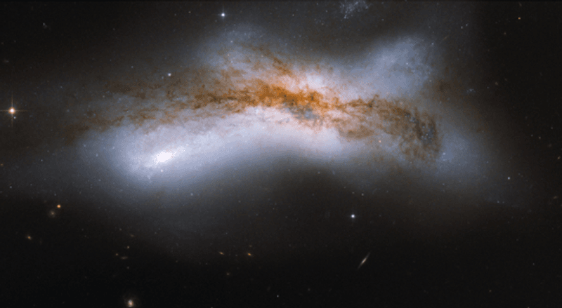 a large dark band of celestial dust is visible against the brigher fuzziness of a messy collision goin on behind