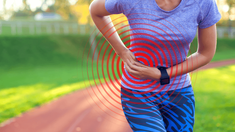 close up photograph of a woman in workout clothing slightly bent over in pain, holding her hand on the side of her abdomen