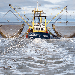 a trawler at sea pulling its nets behind it