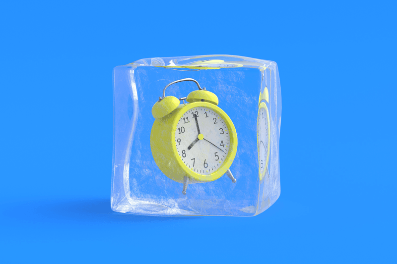 Yellow alarm clock suspended in a cube of ice on a blue background